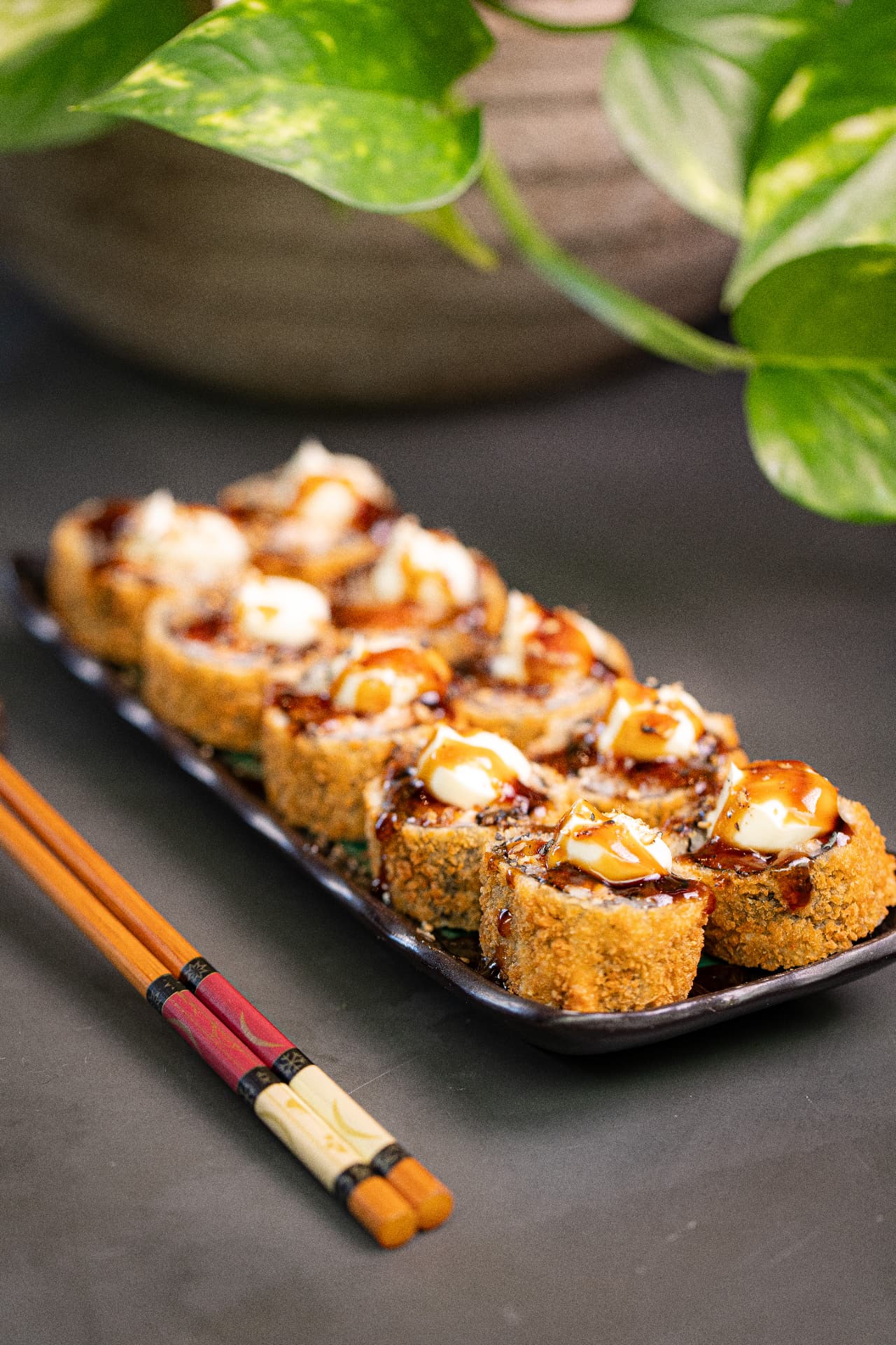 Uramaki frito empanado coberto com molho teriyaki e cream cheese maçaricado, servido em travessa preta