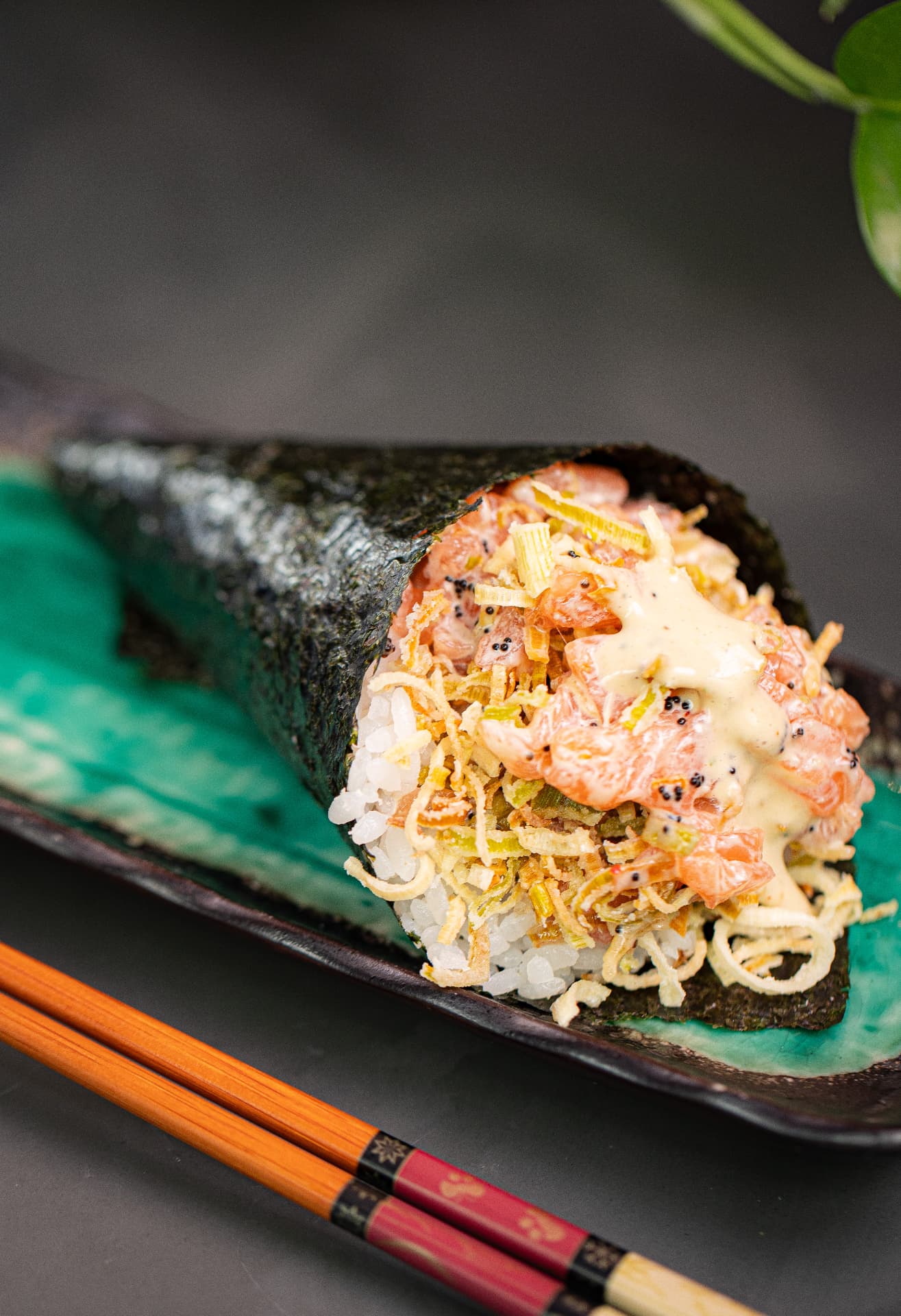 Temaki de salmão com crispy de alho-poró, molho cremoso e ovas, servido em travessa artesanal verde do SAIKO